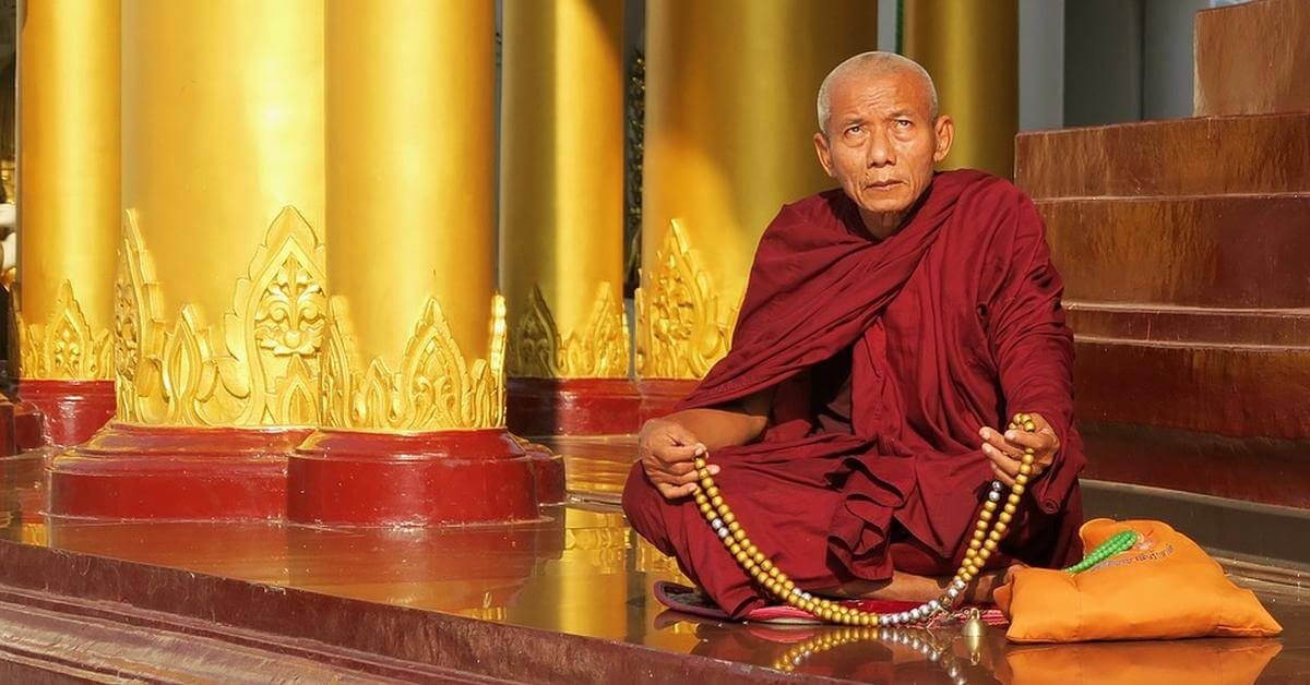 Ein buddhistischer Mönch sitzt auf dem Boden eines Tempelportals.