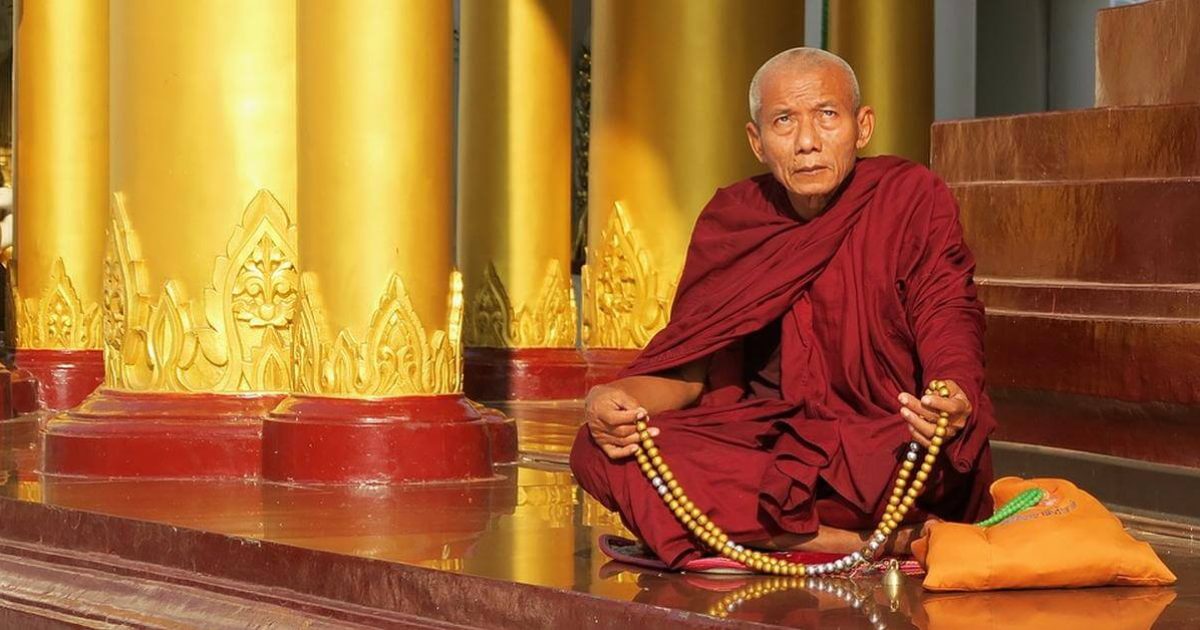 Ein buddhistischer Mönch sitzt auf dem Boden eines Tempelportals.